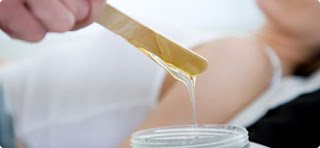 A hand holding a wooden spatula with wax, ready to be applied to a person's arm in the background, reflects the meticulous care at Josephine's Day Spa.