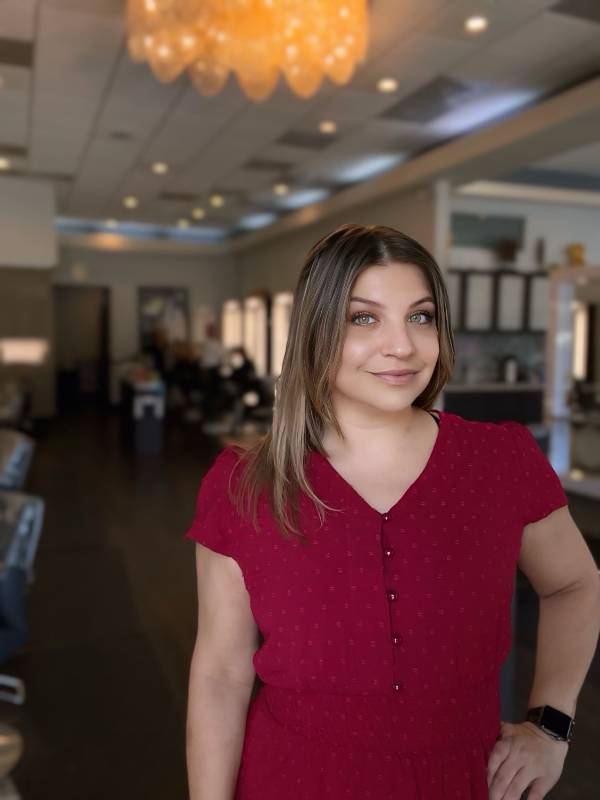 A woman in a red dress stands in a well-lit room with a modern interior and chandeliers, her hair beautifully styled with balayage and highlights.