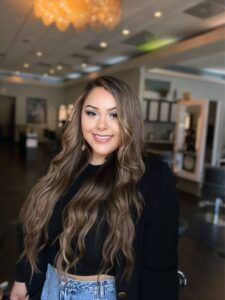 Nicole Pineda, with long wavy hair and a black top, smiles warmly in a salon setting. | Josephine's Salons and Spas