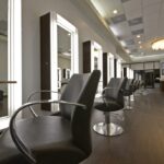 eldridge-10 A modern hair salon with empty black chairs in front of illuminated mirrors and a chandelier overhead. | Josephine's Salons and Spas