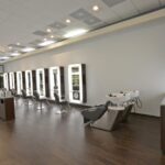 eldridge-12 A modern hair salon with several styling stations featuring mirrors and chairs, along with two wash stations, all set against a neutral interior. | Josephine's Salons and Spas