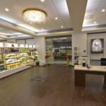 eldridge-2 A spacious, well-lit salon interior with shelves of hair care products on the left and a large desk with computers on the right. A glass entry door is visible in the background. | Josephine's Salons and Spas