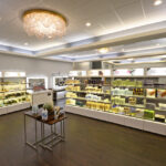 eldridge-3 A well-lit salon interior with shelves displaying various hair and beauty products. A small table stands in the center. Chandeliers hang from the ceiling. | Josephine's Salons and Spas