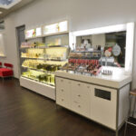 eldridge-4 Beauty store interior featuring illuminated shelves with skincare and haircare products, a makeup display, a large mirror, and a chair on a dark wood floor. | Josephine's Salons and Spas