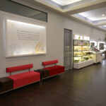 eldridge-7 Modern salon interior with two red bench seats, a display with beauty products, and large mirrors. A sign on the wall describes the salon's services. | Josephine's Salons and Spas