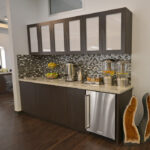 eldridge-8 Modern kitchen area with dark cabinets, mosaic tile backsplash, and granite countertop. Contains fruit baskets, coffee maker, water dispenser, and decorative geode stones. | Josephine's Salons and Spas