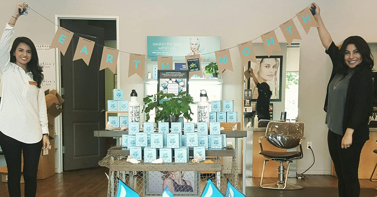 Two women are holding up a "Earth Month" banner inside Josephine's Day Spa. The interior is decorated with products and informational displays, including a plant centerpiece.