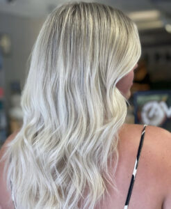 Person with long, wavy, platinum blonde hair that cascades in perfect waves, viewed from the side. Wearing a thin-strap top. Background is blurred. | Josephine's Salons and Spas