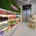 rice-village-4 Brightly lit beauty store interior in Rice Village, with shelves displaying assorted skincare products. A green wall adorned with a neon sign and a small product display table add charm to this shopping destination. | Josephine's Salons and Spas