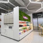 rice-village-8 Located in Rice Village, this modern interior features geometric lighting, a marble counter, and shelves showcasing colorful bottles. A green wall boasts a neon love-themed sign. With its high ceilings and minimalistic decor, it's a shopping haven in the heart of Houston. | Josephine's Salons and Spas