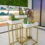 rice-village-9 In the vibrant atmosphere of Rice Village, a haircare product display features green bottles elegantly arranged on white tables. A neon sign and a photo of two women add flair to this Houston shopping experience. | Josephine's Salons and Spas