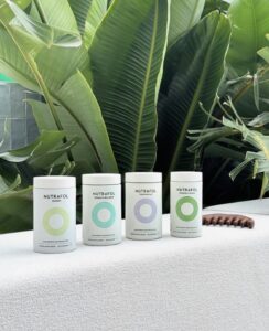 Four Nutrafol bottles on white at a luxury Houston Aveda salon & spa, framed by lush green leaves—beauty and wellness support. | Josephine's Salons and Spas | Houston, TX
