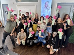A stylish group poses indoors at Josephine’s Salon and Spa in Houston, TX, each with perfect Aveda hair, holding cups with pink tissue paper, showcasing luxury salon services. | Josephine's Salons and Spas | Houston, TX