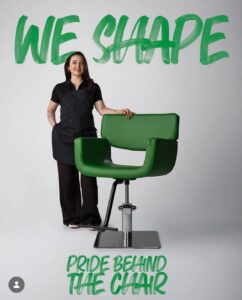 Hairstylist by a salon chair with “WE SHAPE” and “PRIDE BEHIND THE CHAIR” branding at a luxury Aveda salon and spa in Houston, TX, showcasing sustainable beauty. | Josephine's Salons and Spas | Houston, TX